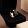Tungsten ring with rose gold polished beveled edges and brushed black center band displayed on black velvet ring stand.